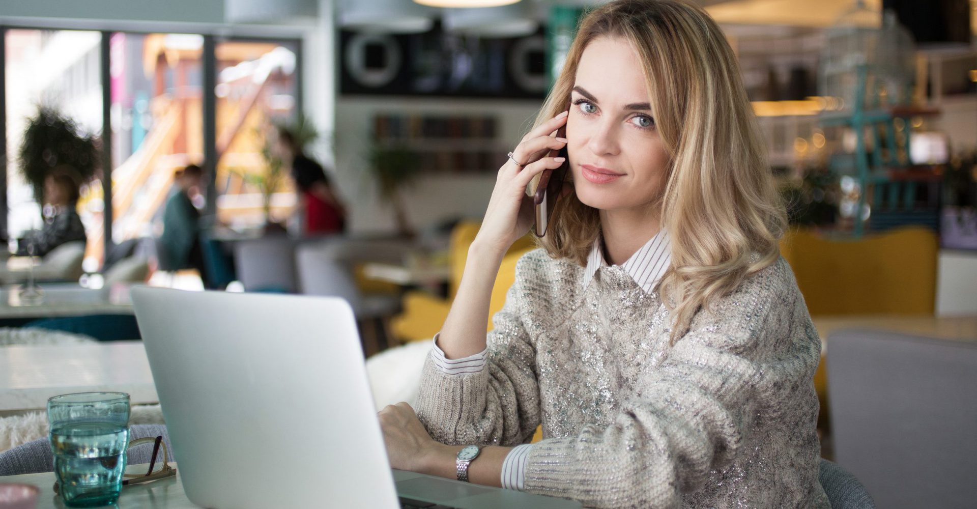 Portrait of beautiful female manager talking on phone. Confident young business lady calling colleague from cafe. She sitting at table with open laptop and looking at camera. Businesswoman concept